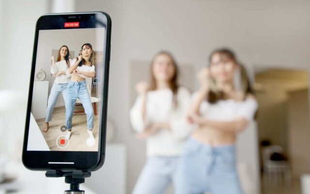 woman in white sleeveless shirt and blue denim skirt holding black smartphone